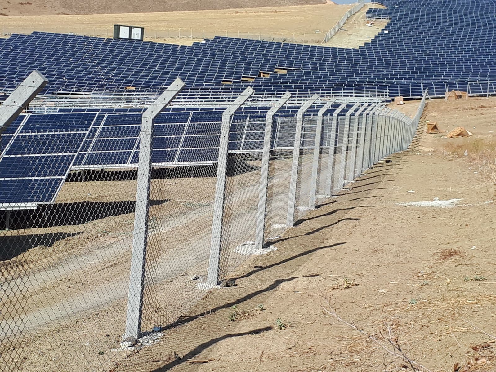 Long concrete post and woven wire mesh perimeter line at a solar power plant