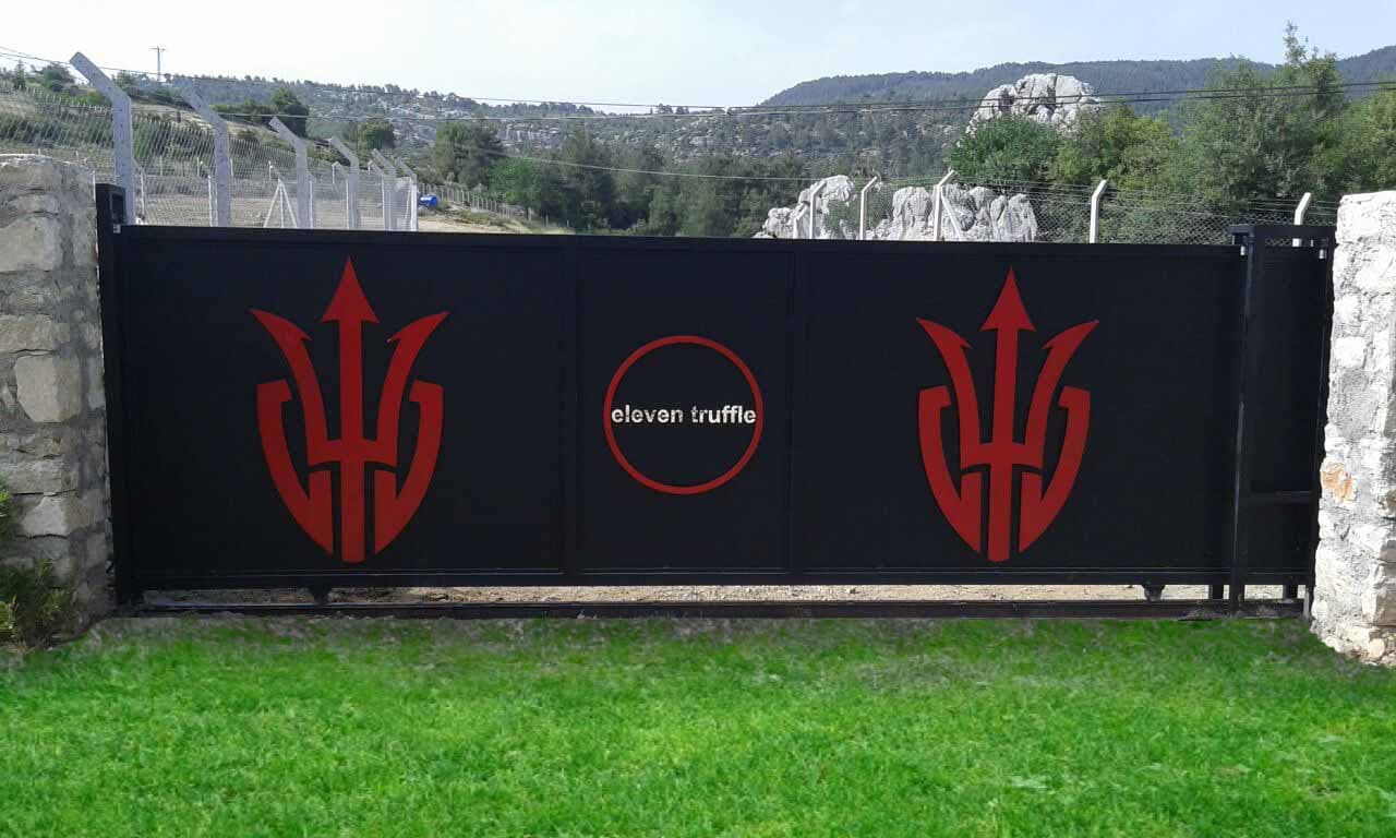 Black sliding entrance gate with a laser cut brand emblem between stone walls