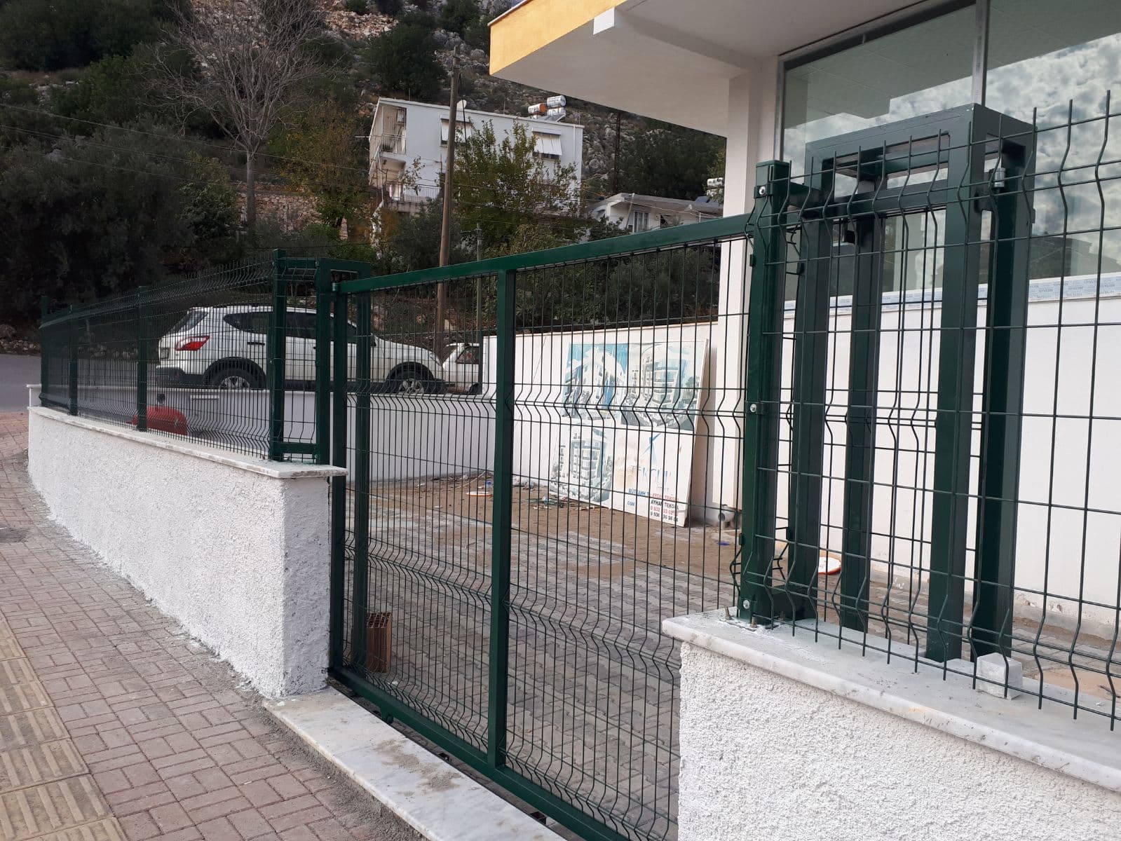 Green welded mesh fence and swing garden gate mounted on a low wall